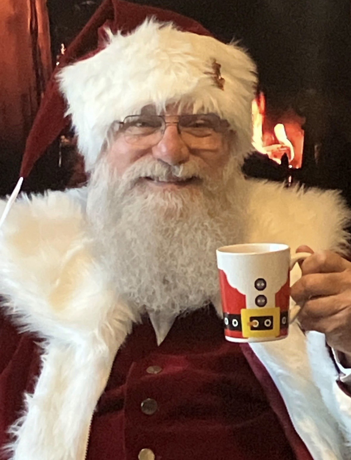 Santa holding a Santa-suit mug by the fireplace