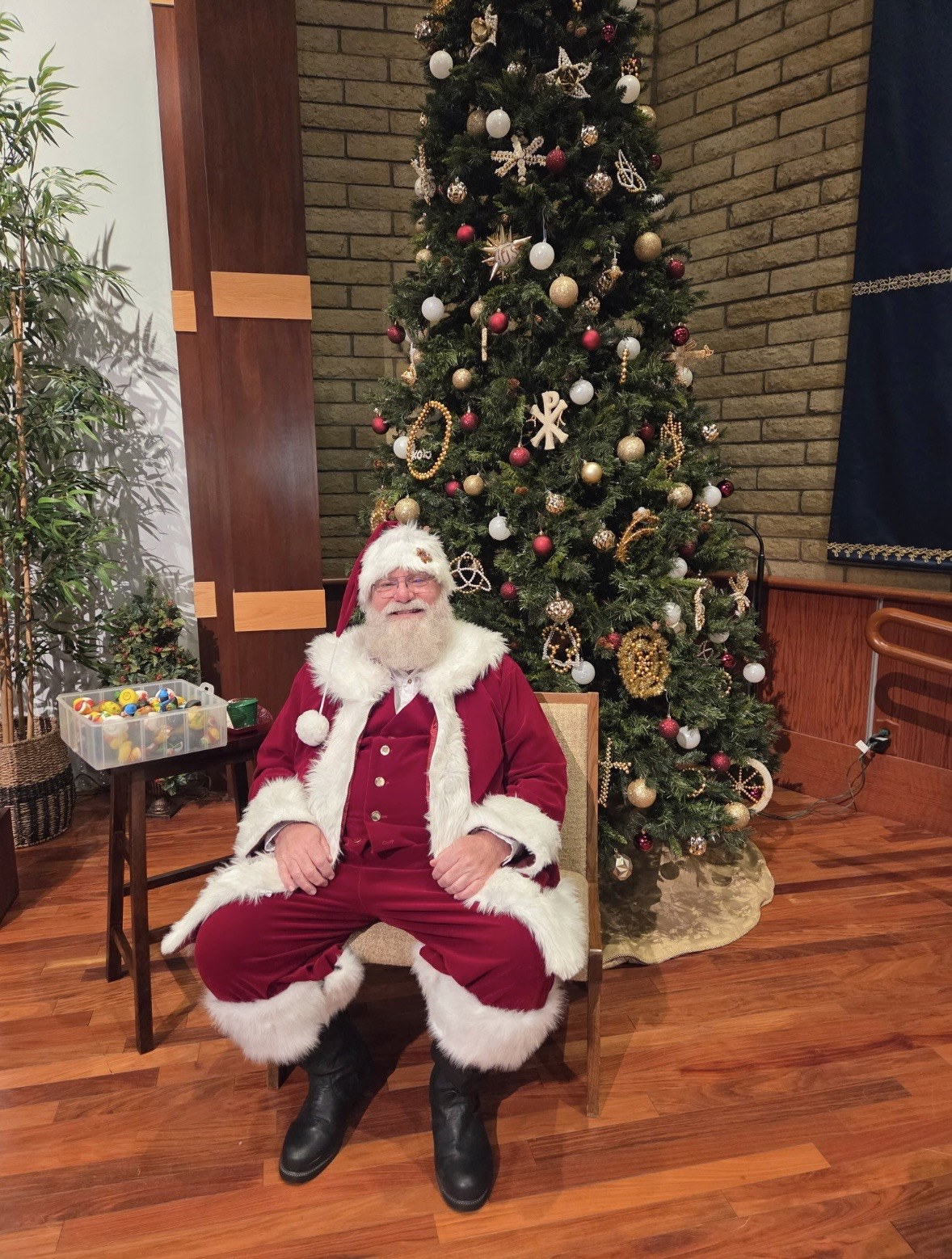 Santa seated beside a tall decorated Christmas tree